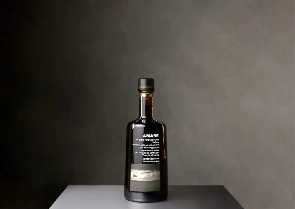 Bottiglia di Olio AMARE con fotografia del mare di Settimio Benedusi sull’etichetta e gocce decorative in peltro lungo il collo.