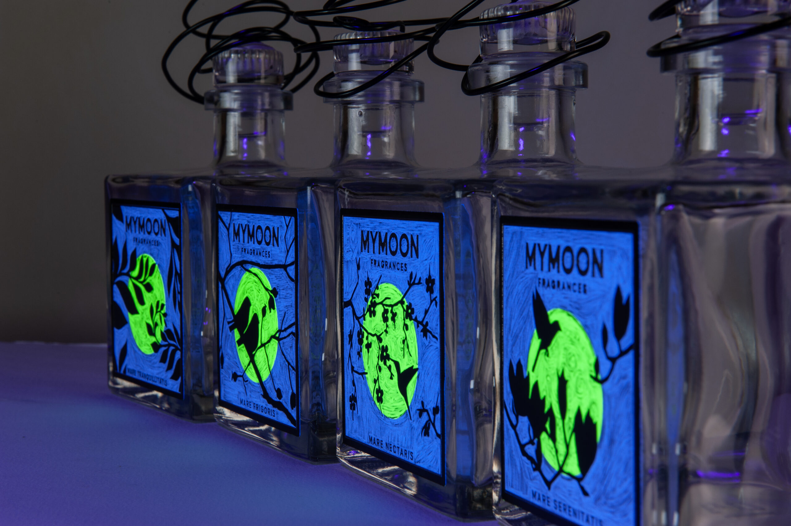 Gli stessi flaconi MYMOON sotto luce UV, con etichette blu e lune fluorescenti.